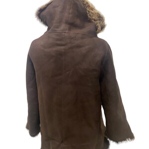 May include: A brown shearling coat with a fur-lined hood. The coat has a long, fitted silhouette and is made of soft, luxurious shearling.