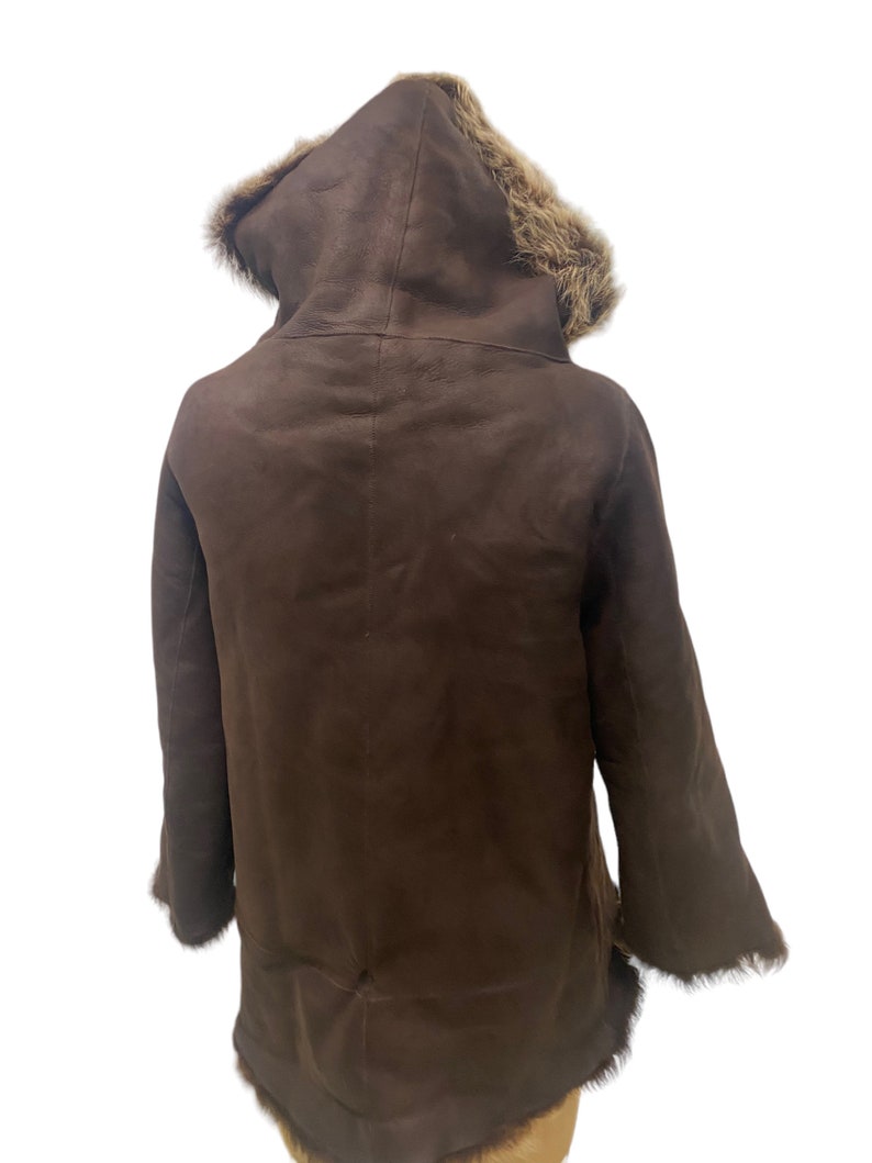 May include: A brown shearling coat with a fur-lined hood. The coat has a long, fitted silhouette and is made of soft, luxurious shearling.