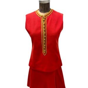 May include: A red sleeveless dress with a gold trim and buttons down the front. The dress has a skirt that flares out at the bottom.
