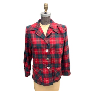 May include: A vintage red and green plaid blazer with three buttons and two front pockets. The blazer is displayed on a mannequin. The plaid pattern is a classic design, and the blazer has a collared neckline.