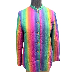May include: A quilted jacket with a vibrant rainbow stripe pattern. The jacket features a mandarin collar, long sleeves, and wooden buttons down the front. The jacket is displayed on a mannequin.