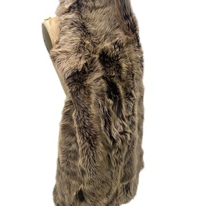 May include: A brown sheepskin rug with long, soft fur. The rug is folded in half and displayed on a mannequin.