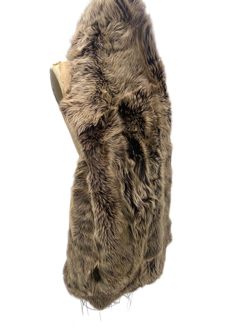 May include: A brown sheepskin rug with long, soft fur. The rug is folded in half and displayed on a mannequin.