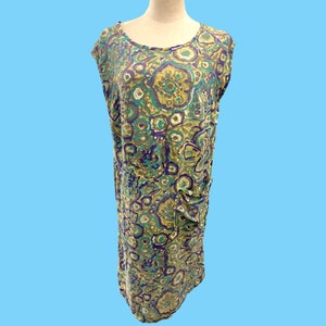 May include: A sleeveless dress with a green, purple, and white abstract floral print. The dress has a scoop neck and a relaxed fit.
