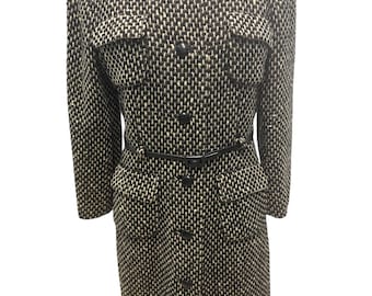 May include: A black, white, and tan patterned coat with a collar, two front pockets, and a black belt. The coat has black buttons down the front and on the pockets. The coat is displayed on a mannequin.
