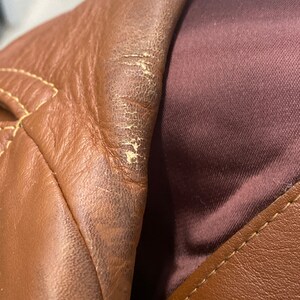 Peut inclure: Gros plan sur une veste en cuir marron avec une doublure marron. Le cuir a une surface textur&eacute;e et montre des signes d'usure.