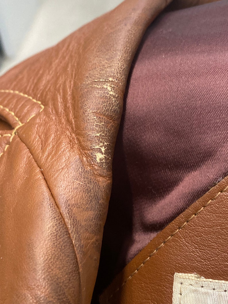 Peut inclure: Gros plan sur une veste en cuir marron avec une doublure marron. Le cuir a une surface textur&eacute;e et montre des signes d'usure.