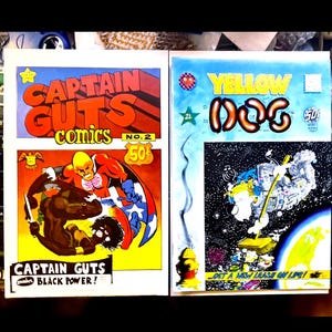 May include: Two vintage comic books are displayed. The left comic is "CAPTAIN GUTS comics NO. 2" with a superhero illustration. The right comic is "YELLOW DOG" with a space-themed illustration. Both comics are priced at 50¢.