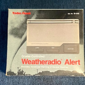 May include: A Radio Shack Weatheradio Alert box, catalogue number 12-240. The packaging features a graphic of a tornado and a silver weather radio with buttons labelled Alert, Test, and Weather. The text reads Crystal-Controlled Weatheradio Alert.