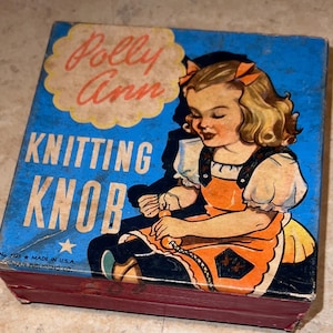 May include: A vintage box for a Polly Ann Knitting Knob toy. The box is blue with a white cloud and the words "Polly Ann Knitting Knob" in red and black lettering. The box features a girl in a red and orange dress knitting with a yellow yarn.