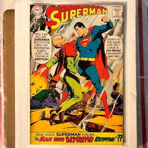 May include: A framed vintage Superman comic book cover. Superman, in a blue suit with a red cape, punches a bald villain in a green and red outfit. Text includes "Superman" and "The Man Who Destroyed Krypton!??"