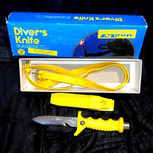 May include: A Z-Lock diver's knife set featuring a stainless steel blade with a bright yellow molded handle, a matching yellow sheath, and a yellow rubber leg strap. The items are presented in a blue cardboard box with white text and graphics.