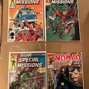 May include: Four comic books, all featuring the Marvel Comics logo. The first three are G.I. Joe Special Missions comics, with the first issue featuring a green-clad soldier holding a gun, the second issue featuring a soldier in a red jumpsuit falling from the sky, and the third issue featuring a blue van with soldiers standing around it. The fourth comic is Nomad, Captain America, stepping from the pages of America, featuring a man with long black hair and a black and white costume.