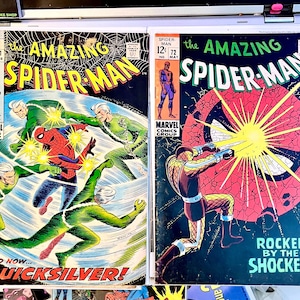 Op de afbeelding: Twee vintage strips van "The Amazing Spider-Man", nummers #71 en #72. Nummer #71 toont Spider-Man en Quicksilver, terwijl #72 Spider-Man en de Shocker laat zien. De strips zijn van de Marvel Comics Group.