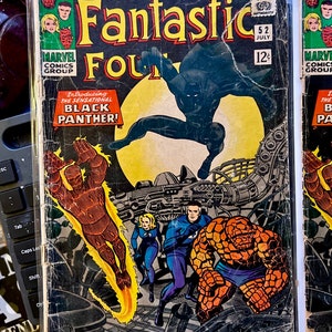 May include: A vintage comic book cover of Fantastic Four #52, featuring the Black Panther. The cover art includes the text "Introducing the Sensational Black Panther!" and the Marvel Comics Group logo. The comic is in a protective sleeve.