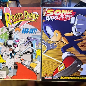 May include: Two comic books, one featuring Roger Rabbit painting with a paintbrush and the other featuring Sonic the Hedgehog in a fighting pose. The Sonic comic book is titled "Sonic Worlds Unite: Battles" and is a variant cover. The Roger Rabbit comic book is titled "Roger Rabbit Rub-Out!" and is issue number 2.