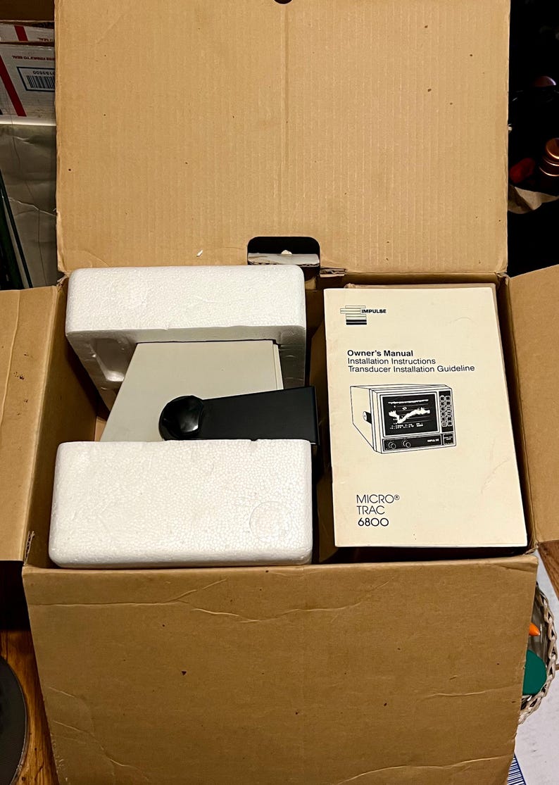 May include: A cardboard box containing a piece of electronic equipment secured with white styrofoam packaging. Next to the equipment is a manual titled Impulse Owner's Manual, Installation Instructions, Transducer Installation Guideline, MICRO TRAC 6800.