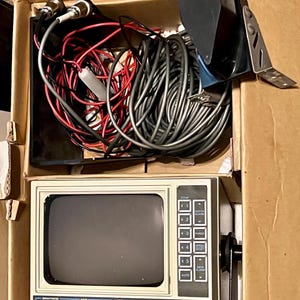 May include: An Impulse Micro-Trac 6800 fish finder unit with a beige casing, a dark screen, and a control panel featuring buttons and knobs. The unit is packed in a cardboard box with a bundle of gray and red electrical cables and a black transducer.