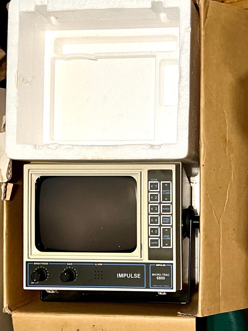 May include: An Impulse Micro-Trac 6800 fish finder with a beige casing and a black screen. The device features a control panel with buttons labeled Zoom, Depth Alarm, Range, Speed Reset, and Deep Alarm, plus knobs for brightness, gain, and alarm.