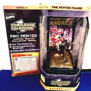 K&ouml;nnte beinhalten: Eine limitierte "Comic Book Champions" Feinzinnfigur von Captain America, pr&auml;sentiert in einer transparenten Kunststoffbox. Die Figur steht auf einem goldfarbenen Sockel mit offenem Buchdesign. Die Verpackung enth&auml;lt den Text "Golden Age" und "Marvel Comics".