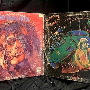 Puede incluir: Dos álbumes de discos de vinilo vintage. El álbum de la izquierda es rojo con el texto "Ssssh. Ten Years After" y un retrato. El álbum de la derecha es negro con el texto "A Space in Time" y un hombre tocando la guitarra.