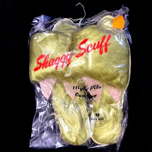 May include: A pair of yellow "Shaggy Scuff" slippers in a clear plastic bag. The slippers have a high-pile texture and pink accents. The tag indicates a shoe size of 6 1/2 - 7 1/2.