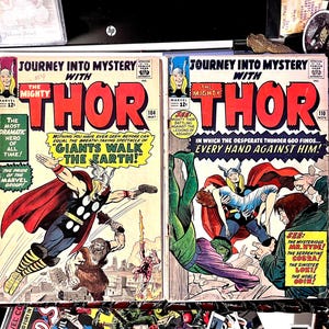 Può includere: Due fumetti vintage "Journey into Mystery" con "The Mighty Thor". Le copertine sono dai colori vivaci con scene d'azione e testo. Una copertina recita "Giants Walk the Earth!" e l'altra "Every Hand Against Him!". Entrambi sono di Marvel Comics.