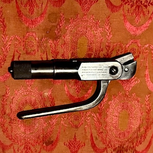 May include: A black antique tool with a lever and a textured handle. The tool has text that reads "Manufactured by The Winchester Repeating Arms Co. New Haven, CT, U.S.A. Feb. 15 1894."
