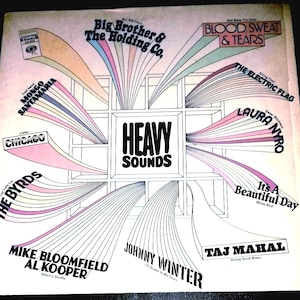 May include: A square vinyl record cover titled Heavy Sounds featuring a central white grid design. Radiating from the center are colorful, fan-shaped graphic elements with black text listing various artists and song titles including Big Brother & The Holding Co., Blood, Sweat & Tears, Chicago, The Byrds, and Taj Mahal.