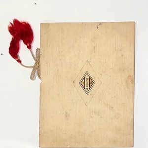 May include: A rectangular off-white paper document with a red tassel attached by a beige cord. The centre features a diamond-shaped emblem containing the text "CLASS 18". The paper shows signs of age with light discoloration and surface texture.