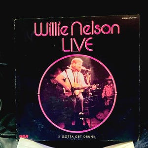 May include: A vintage vinyl record album cover for Willie Nelson's "Live" album. The cover is black with pink lettering and a pink circular image of Nelson playing guitar. The text "I GOTTA GET DRUNK" is at the bottom.