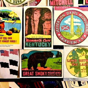 May include: A collection of vintage travel stickers featuring Smokey Bear, Mammoth Cave, the Jefferson Davis Monument, and Great Smoky Mountains National Park. The stickers are rectangular and circular, with colorful illustrations and text.