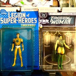 May include: Two DC Direct action figures in original packaging. One is "Legion of Super-Heroes Timberwolf" in yellow and white. The other is "Tomorrow Woman" in green. Both figures are in clear plastic packaging with blue and brown cardboard backings.