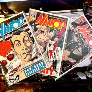 May include: Three comic books featuring the superhero Namor, the Sub-Mariner. The covers are red, yellow, and blue with illustrations of Namor and other characters. The text on the covers reads "Namor, the Sub-Mariner".