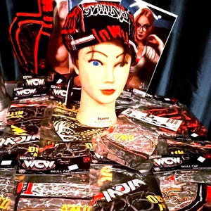 May include: A display of skull caps with a black and red design, some in clear plastic packaging. A mannequin head with blue eyes and red lipstick wears a skull cap. The text "WOW" and "SKULL CAP" are visible.