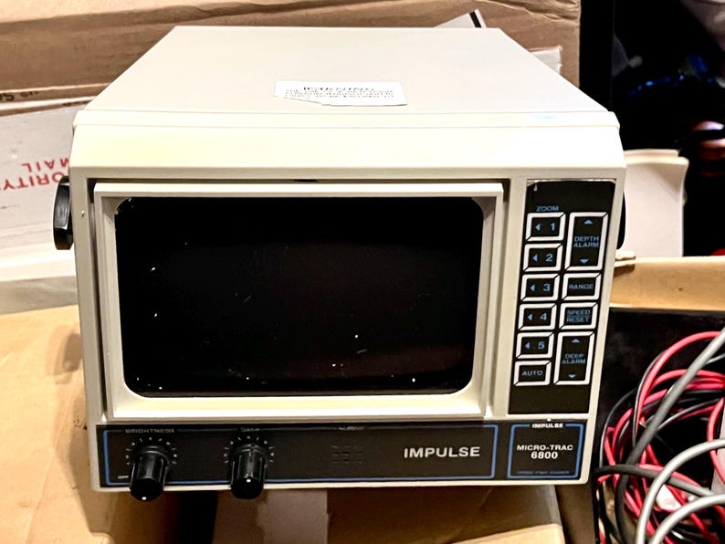 May include: An off-white Impulse Micro-Trac 6800 marine sonar display unit featuring a dark screen, a vertical control panel with numbered buttons, depth and range settings, and two black rotary knobs for brightness and gain control on the front.