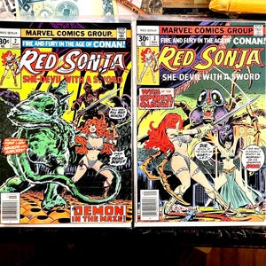 May include: Two vintage comic books featuring "Red Sonja: She-Devil with a Sword." The covers showcase action-packed scenes with vibrant colors, including a red-haired warrior, monsters, and the text "Demon in the Maze!" and "Web of the Spider Queen!"
