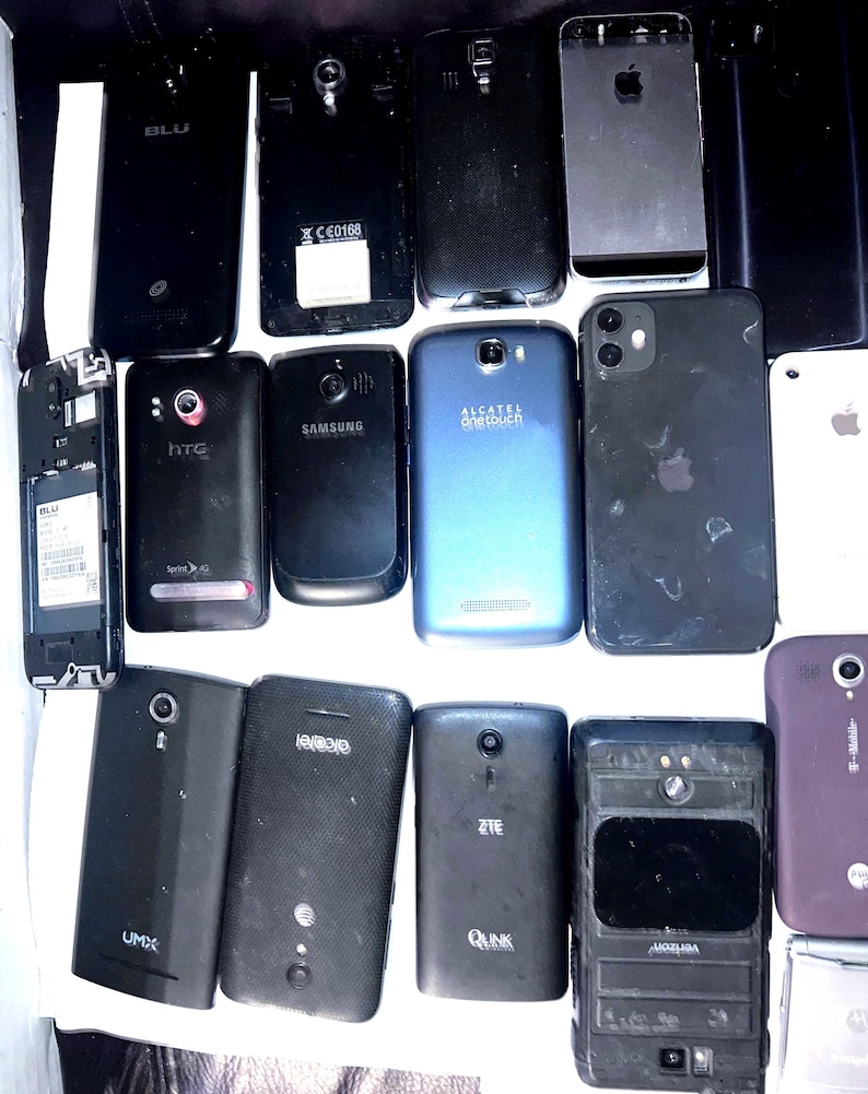 May include: A collection of various used smartphones, including brands like Apple, Samsung, and HTC. The phones are primarily black, with some blue and silver accents. Some phones have visible logos and model names.