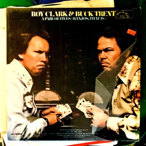 May include: Album cover for "Roy Clark & Buck Trent - A Pair of Fives (Banjos, That Is)". The cover features two men holding playing cards. The album title and artist names are visible. The album is a vintage vinyl record.