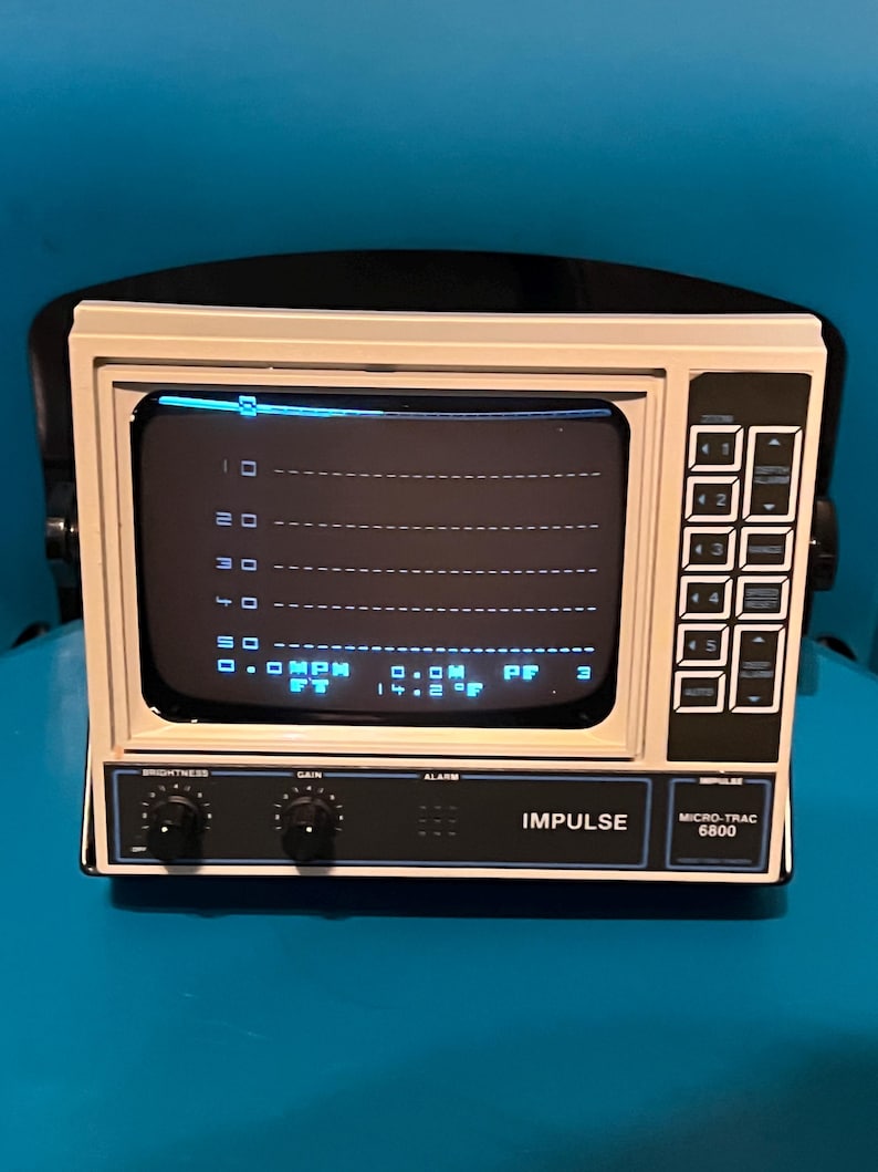 May include: An Impulse Micro-Trac 6800 monitor with a beige casing and a black control panel. The screen displays a digital interface with horizontal grid lines, numerical data, and text including MPH, FT, and 14.2 degrees Fahrenheit.