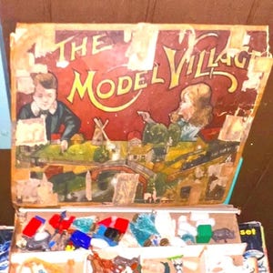 May include: Vintage "The Model Village" set with a colorful box featuring illustrations of children and a village scene. The box opens to reveal compartments filled with miniature plastic figures and accessories, perfect for imaginative play.