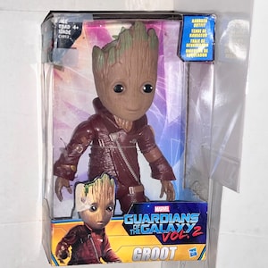 May include: A plastic action figure of Groot from Guardians of the Galaxy Vol. 2. The figure is wearing a brown leather jacket and has a green leafy head. The packaging is yellow and blue with the Marvel logo and the movie title.