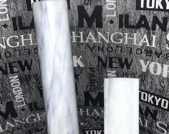 May include: A white marble rolling pin with a wooden handle and a white marble rectangular block. The background is a black and white fabric with city names printed on it.