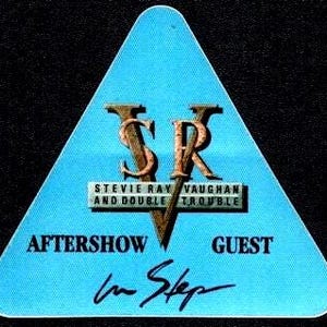 May include: A light blue, triangular guitar pick featuring the initials "SRV" in a copper color, with the text "STEVIE RAY VAUGHAN AND DOUBLE TROUBLE" below. The words "AFTERSHOW" and "GUEST" flank the text, and "In Step" is written in cursive.