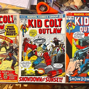 Op de afbeelding: Drie vintage stripboeken met het personage Kid Colt Outlaw. De omslagen zijn in kleur en bevatten illustraties van cowboys en vuurgevechten. De titels van de stripboeken zijn "Kid Colt Outlaw", "Kid Colt Outlaw" en "Kid Colt Outlaw".