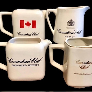 May include: Four white ceramic pitchers with the "Canadian Club" logo and text. One pitcher features the Canadian flag. Other pitchers have the text "Whisky", "Imported Whisky", and "The Best in The House".