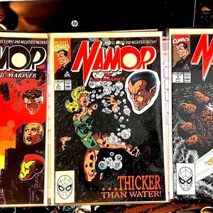May include: Three comic books featuring the superhero Namor, The Sub-Mariner. The covers are black, red, and blue with images of Namor in different poses. The text on the covers reads "Namor, The Sub-Mariner" and "Marvel's First and Mightiest Mutant".