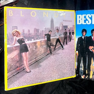 Op de afbeelding: Een vinyl platenhoes met de band Blondie. De hoes toont een groep mensen die op een dak staan voor een stadsbeeld. De albumtitel "Blondie" is gedrukt in grote, gele letters bovenaan de hoes. De ondertitel van het album "Autoamerican" is gedrukt in kleinere, witte letters aan de linkerkant van de hoes.