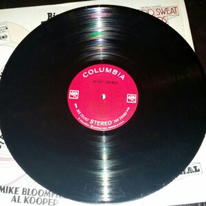 May include: A black vinyl record featuring a circular red center label with white text that reads Columbia, Heavy Sounds, and 360 Sound Stereo. The record is positioned over a white album cover with text including Mike Bloomfield and Al Kooper.