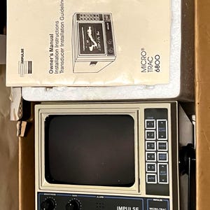 May include: An Impulse Micro-Trac 6800 marine fish finder unit with a beige casing, a black screen, and a control panel featuring buttons and knobs. Included is an owner's manual titled Owner's Manual Installation Instructions Transducer Installation Guideline.
